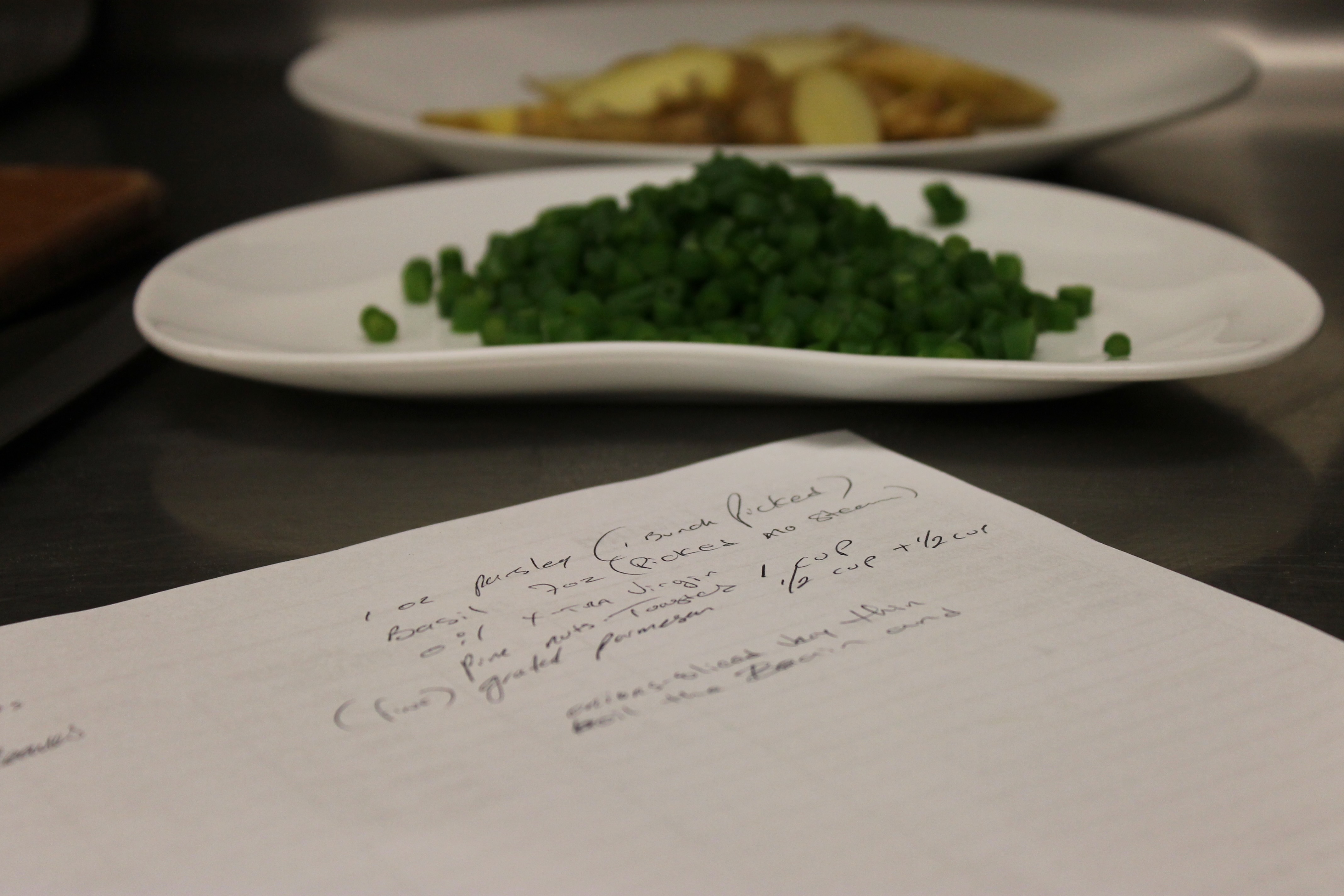 Handwritten recipe notes on a kitchen prep station with mise en place in the background