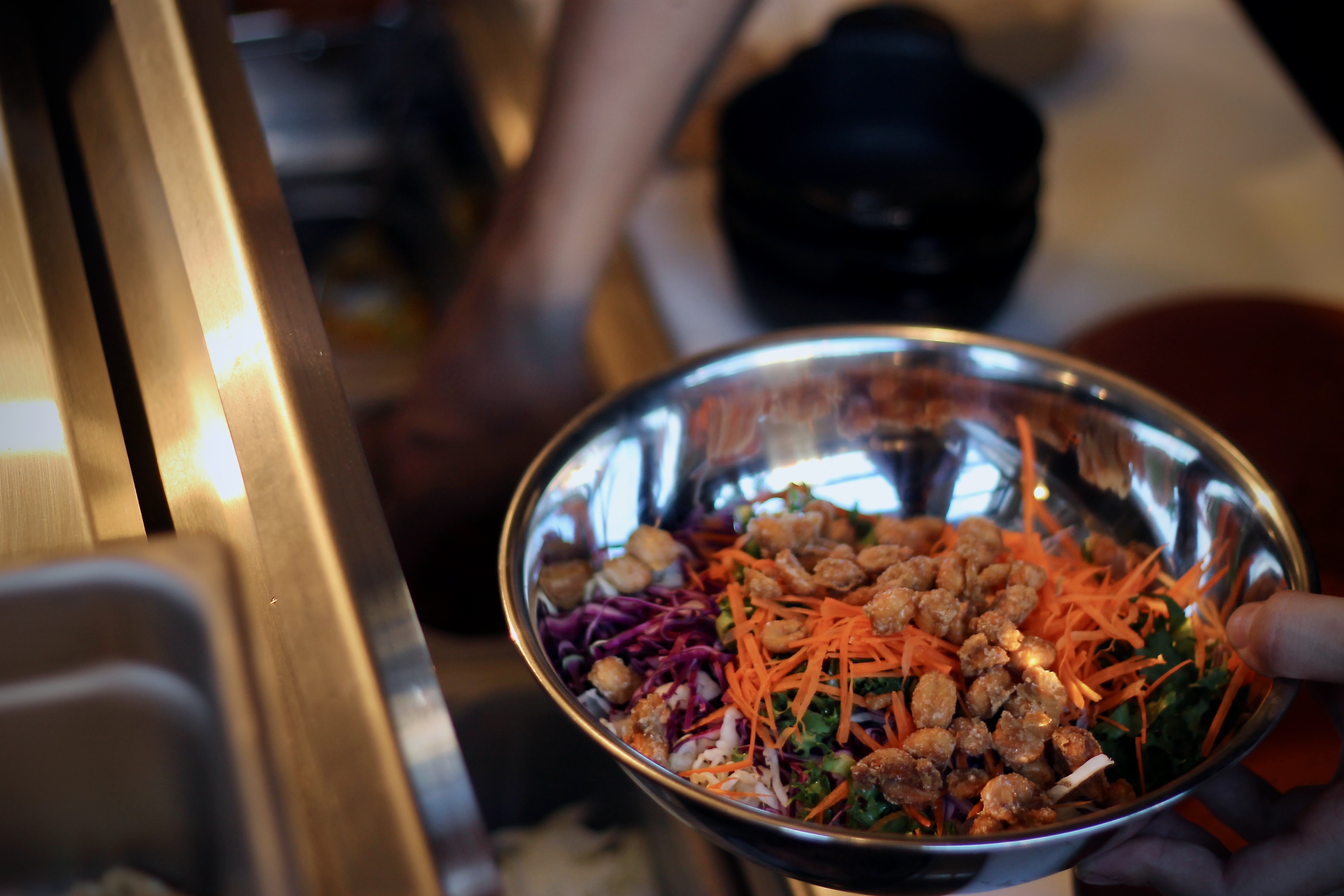 A bowl being assembled at the line, hands at work in a professional kitchen